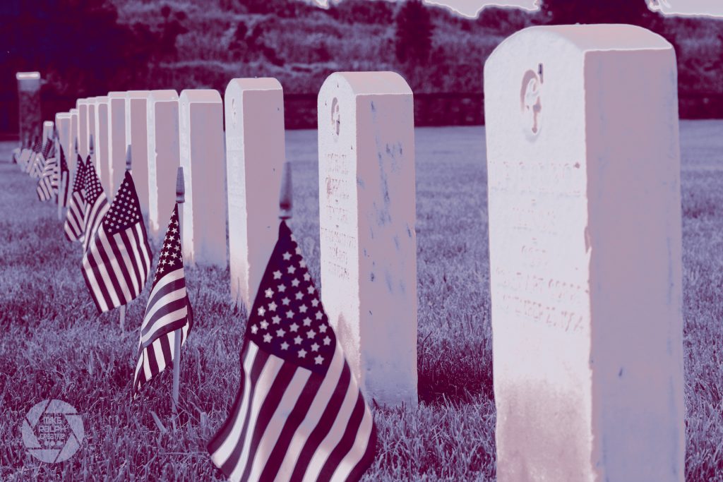 Duotone picture of American flags placed in front of gravestones  